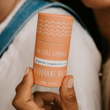 A person holding a deodorant tube with natural approach branding, bergamot grapefruit & lime, in a compact orange casing.